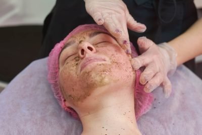 Hands applying coral face peel. Young woman at the cosmetician.